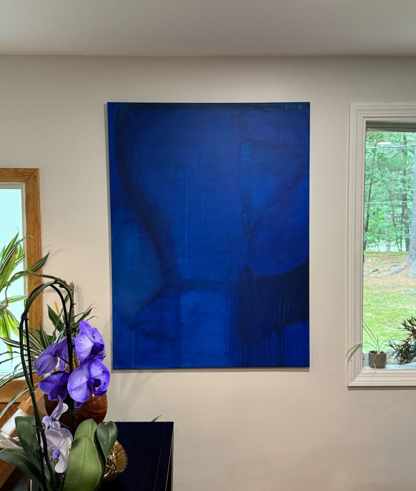 Abstract blue painting hung in home by windows.