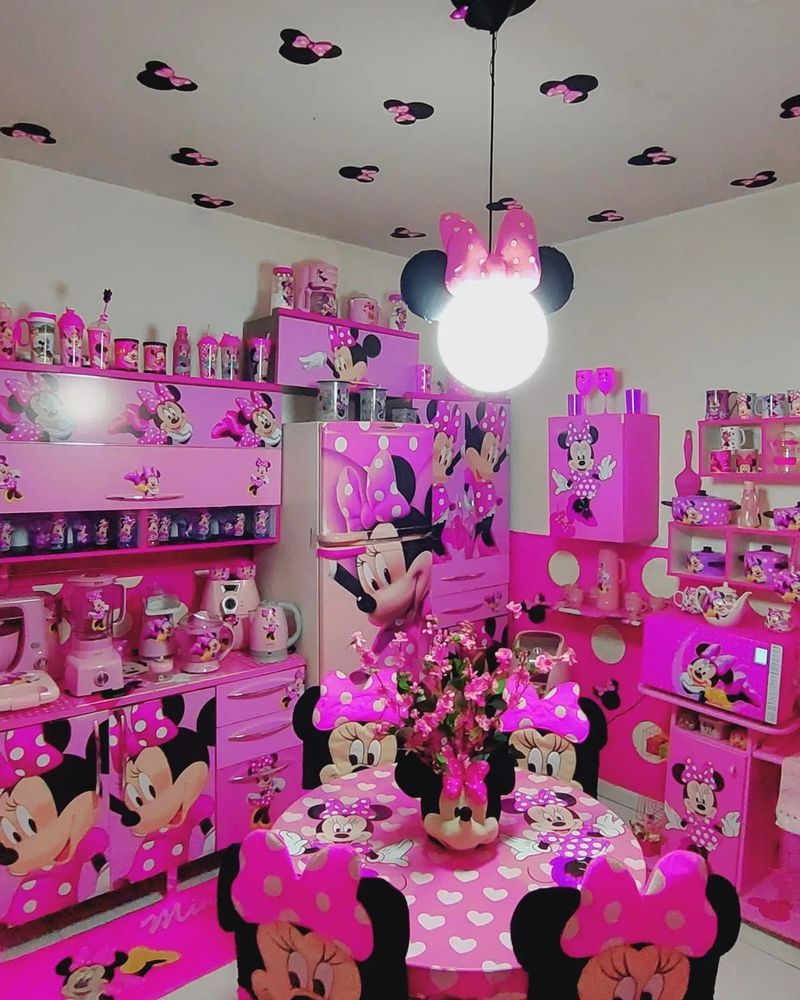Uma cozinha com geladeira, armários, eletrodomésticos, mesa e cadeiras adesivados com uma Minnie de laço rosa