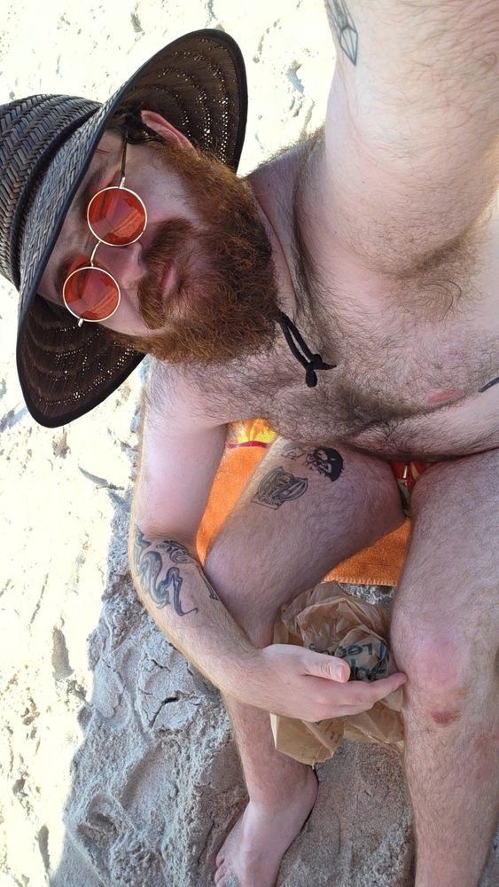 Sitting at the beach in the speedo from the last picture, paired with a sun hat and some orange sunglasses. A publix bag sits between my knees.