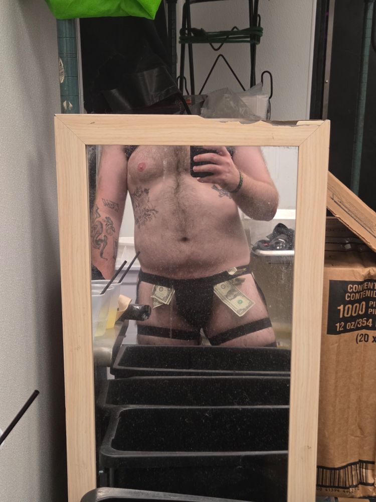 Im standing faceless in a mirror, showcasing a black thong with straps placed throughout it.