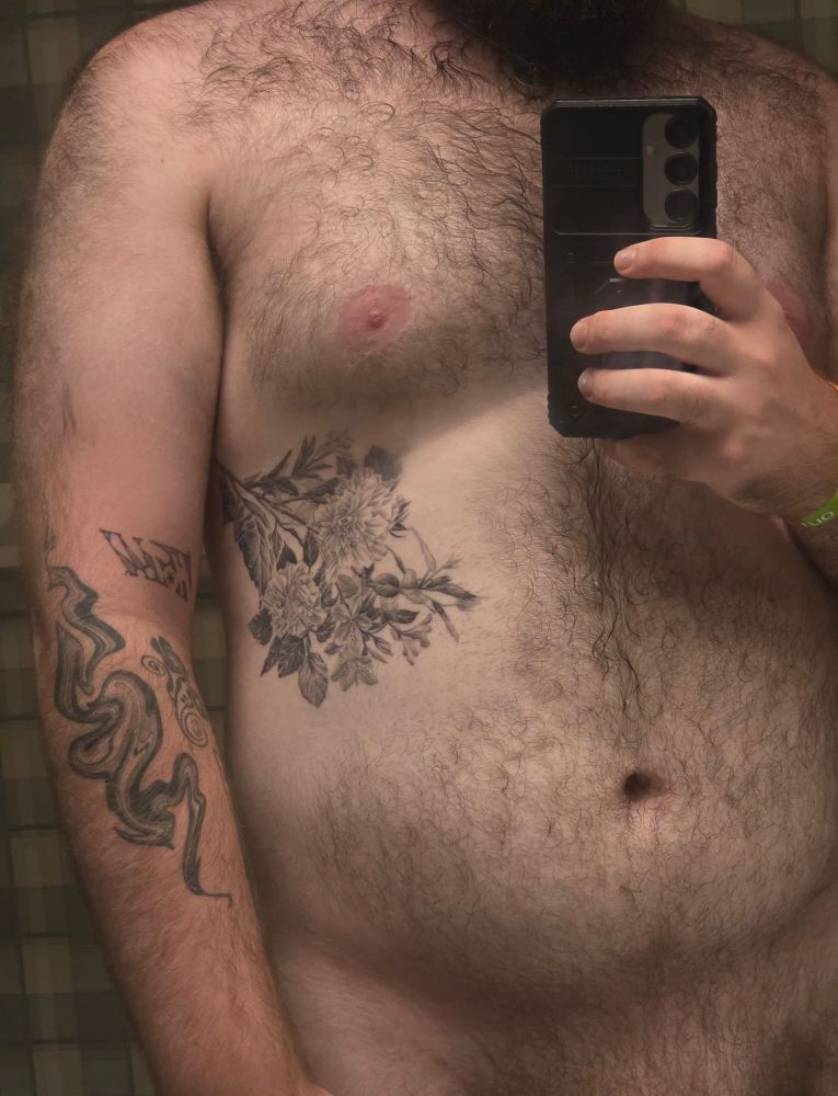 A mirror selfie of my chest and stomach, once again focusing on the flower tattoo on my left rib (and a little bit of bush).