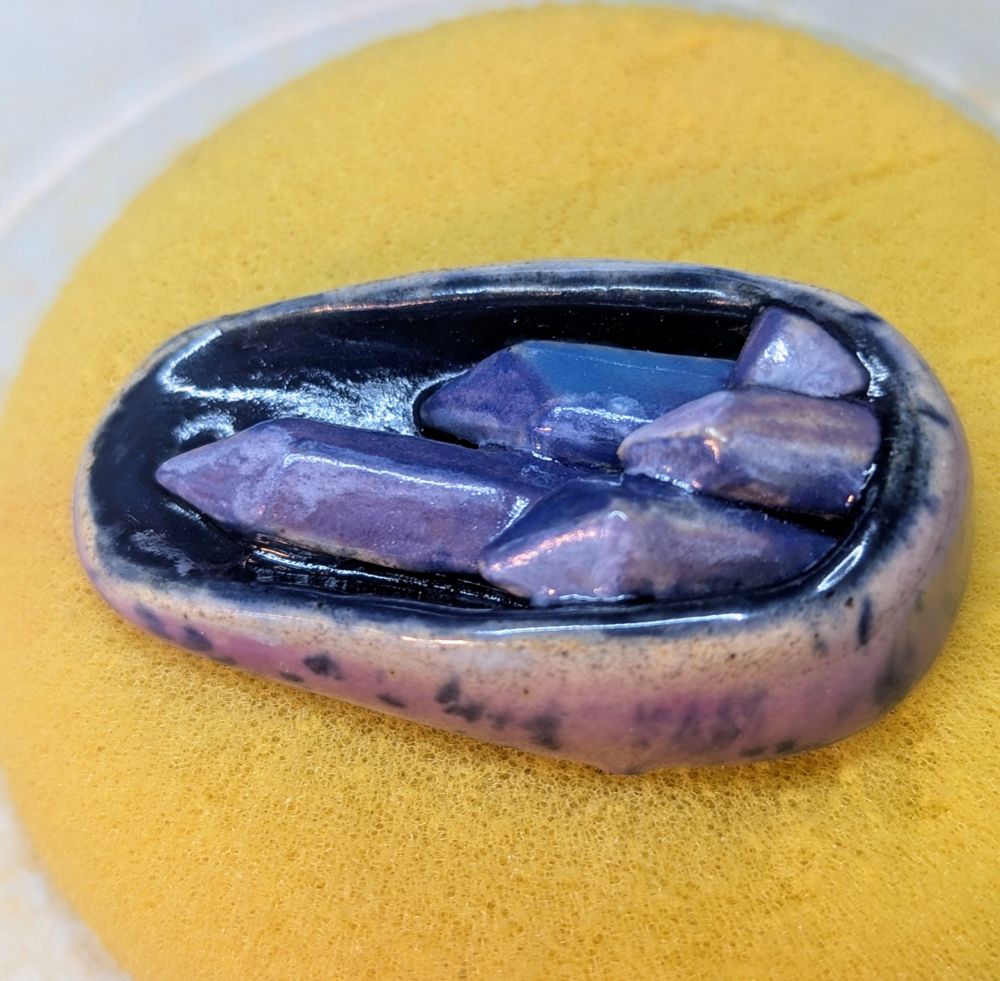 2 inch oval ceramic pendant pockets with mini scenes. One is a green snake with yellow/orange sun and one is a dark background with 5 crystals in purples. 