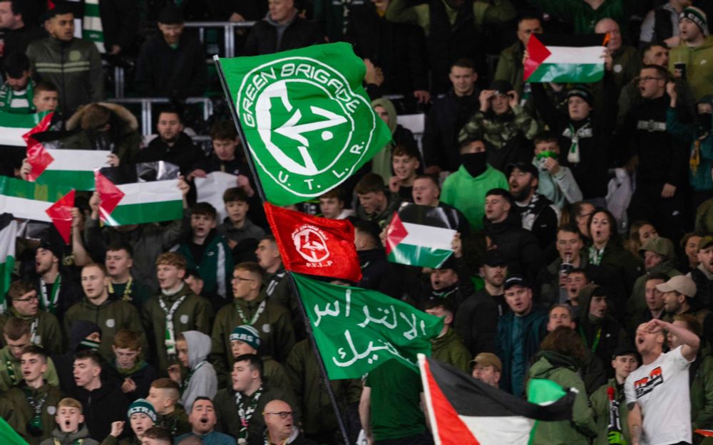 Celtic FC supporter waving militant flags in support of Palestine with other supporters with Palestinian flags in the background