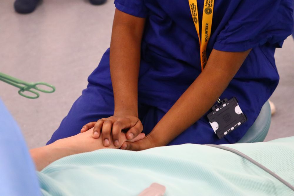 A close-up on a volunteer in scrubs holding hands with a patient lying on a bed. 