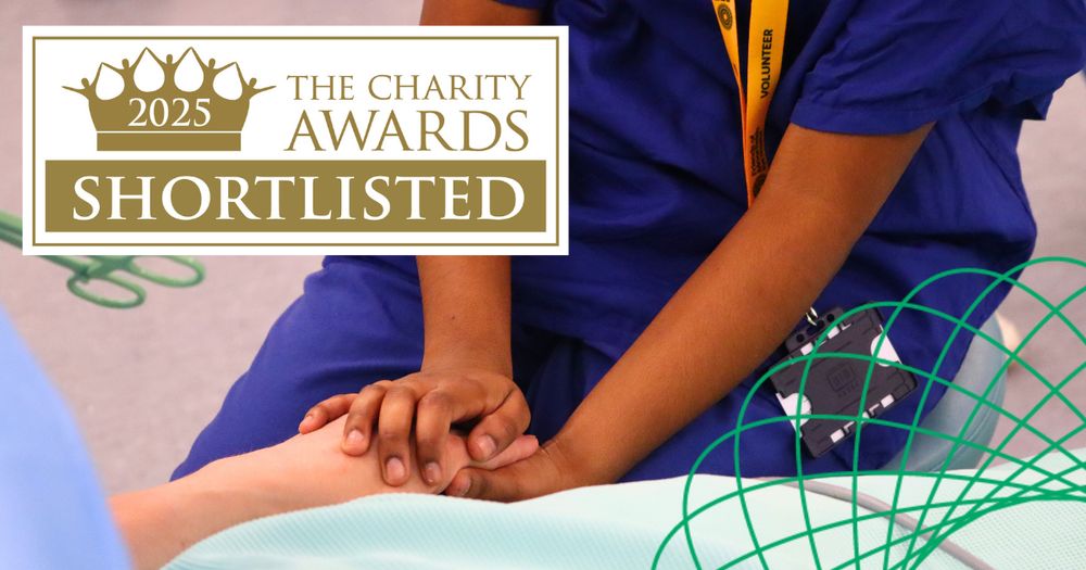 A close-up of a volunteer in scrubs holding a patient's hand. Text reads: 2025 - The Charity Awards - Shortlisted.