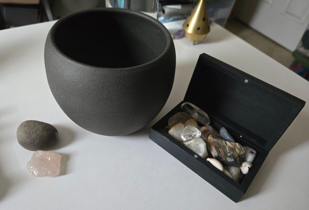 A picture of a small stoneware pot typically used for plants. It's sitting next to an assortment of stones on a desk.