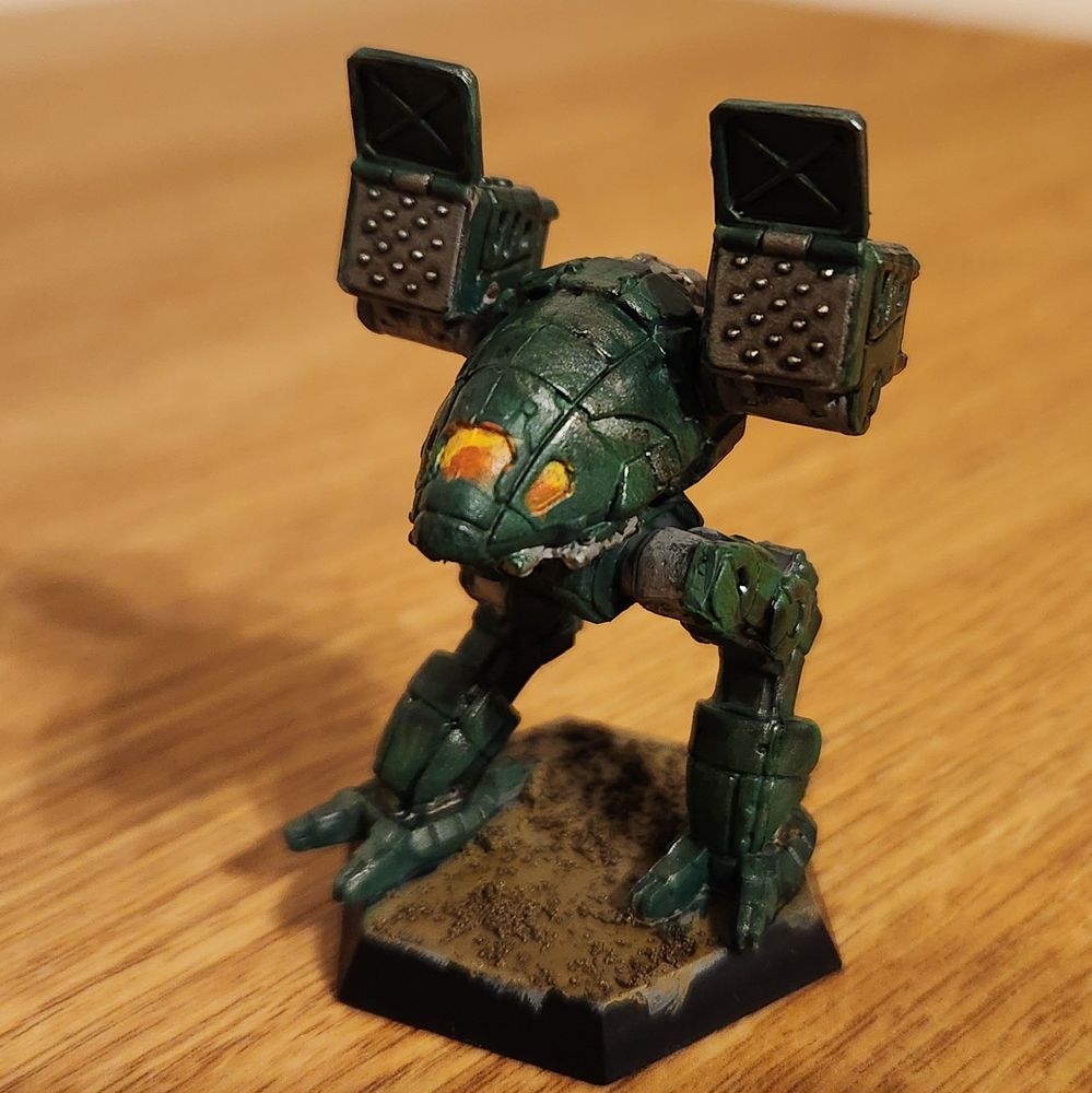 A miniature of a Catapult mech from Battletech, painted dark green, with an orange and yellow cockpit, and silver metallics throughout.