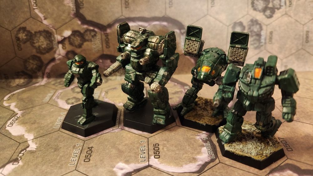 A lance of four battlemechs from battletech, all painted in the same dark green, with various amounts of weathering and oil stains, and orange/yellow cockpits. From left to right is a Commando, an Awesome, a Catapult, and a Wolverine.