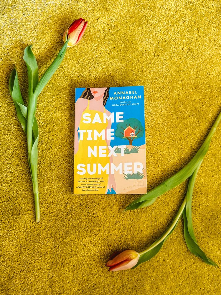 The book Same Time Next Summer by Annabel Monaghan on a yellow carpet with tulips 