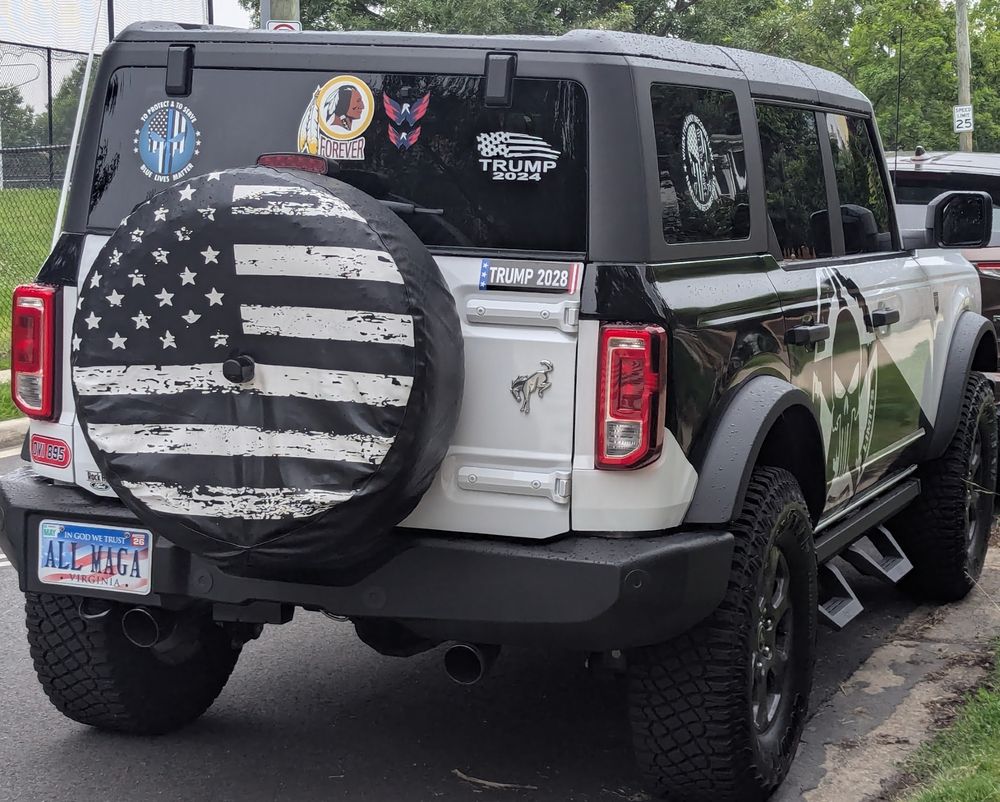 A Ford Bronco covered in Trump stickers and Punisher stickers, plus the Punisher skull painted on the side. The license plate reads ALL MAGA.
