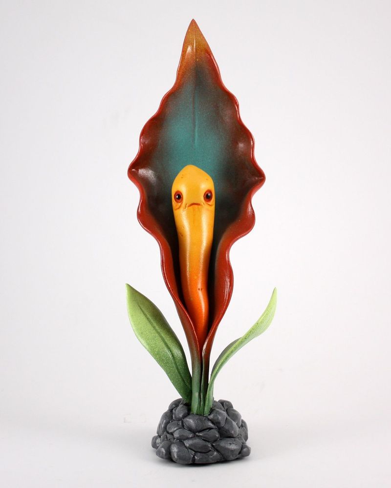 Photo of an orange and red Bloom Blight sculpture of a flowering plant with green leaves and a grey rock base, by Andrew Bell
