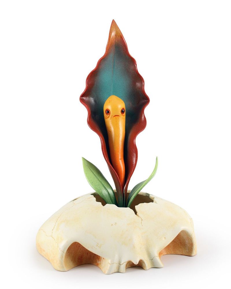 Photo of an orange and red Bloom Blight sculpture of a flowering plant with green leaves coming out of a cracked monster skull, by Andrew Bell