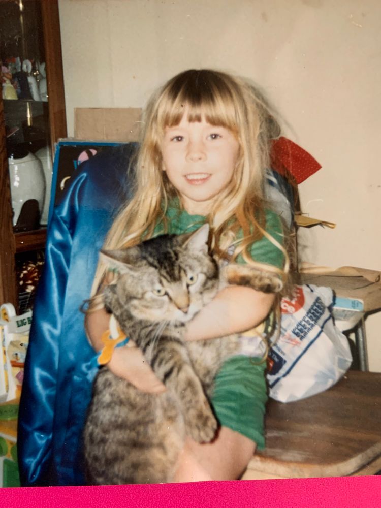 A photo of a young, blond alonechark holding a big stripey cat that is basically half of her size.