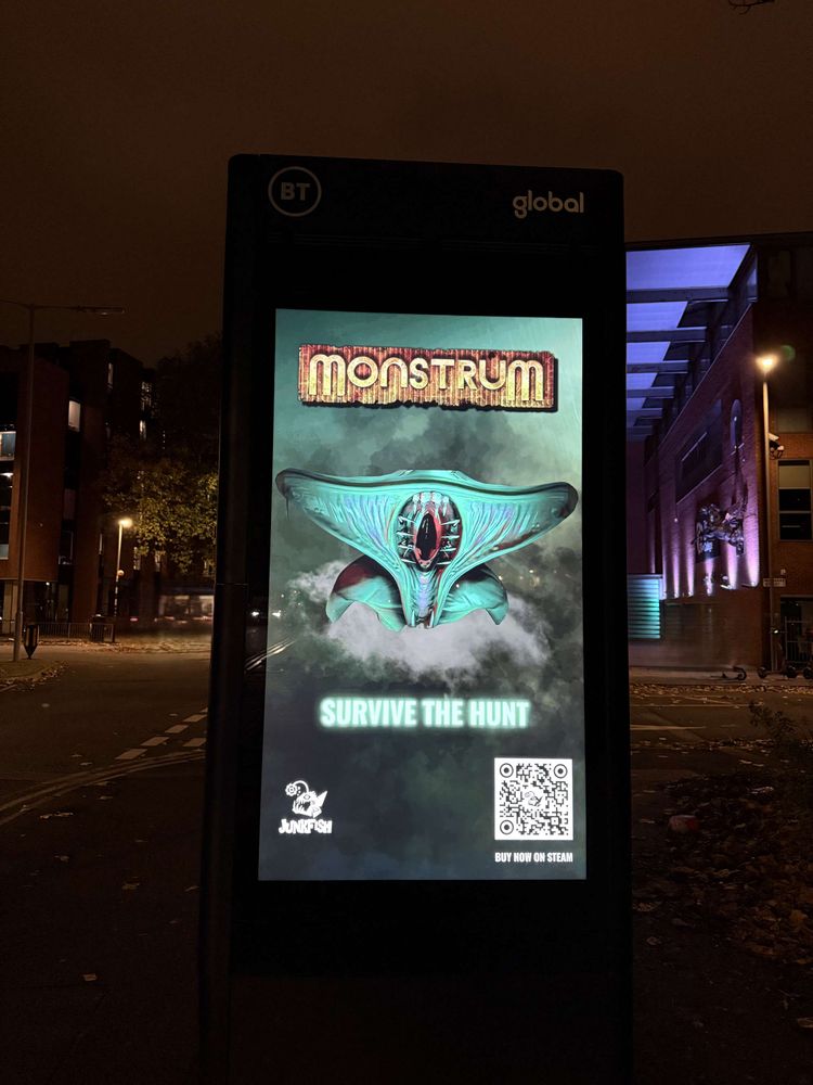 A picture of a advertising screen in a city centre, on thee screen is a monstrum advert showing the Hunter monster and the text "survive the hunt" with a team junkfish logo and QR code that links to the game on steam