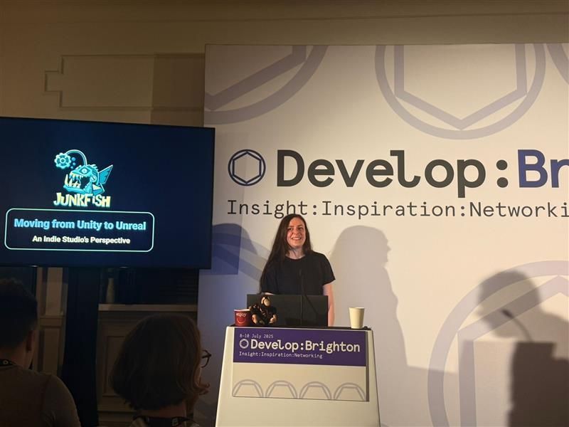A speaker presenting at the Develop:Brighton conference, with a screen displaying "Junkfish" and the topic "Moving from Unity to Unreal."