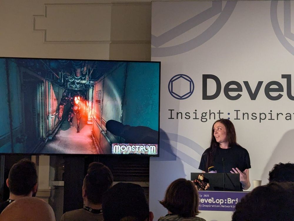 A presenter stands at a podium displaying a dark game scene on screen, showcasing a tense moment from the game "Monstrum."