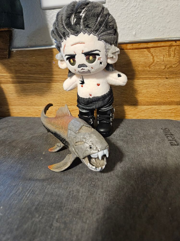 15 cm Izzy doll by imrights dressed in jeans and biker boots. He's standing on a draining board with a dunkleosteous toy next to him. 