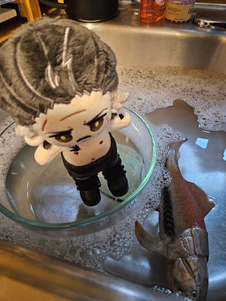 15 cm Izzy doll by imrights dressed in jeans and biker boots. He's floating in a pyrex dish in a kitchen sink with a dunkleoteus toy