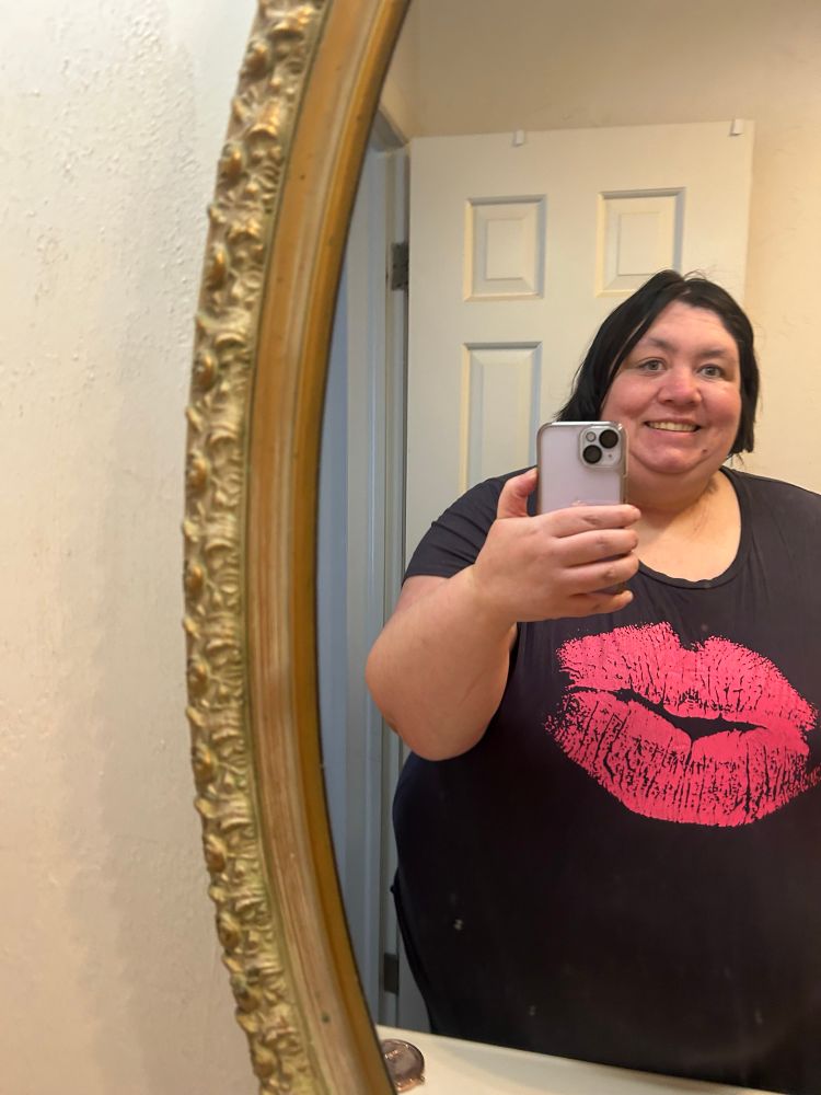 Mirror selfie, showing off my new haircut. Wearing a grey shirt with a pink kiss print on it, holding a lavender colored phone.