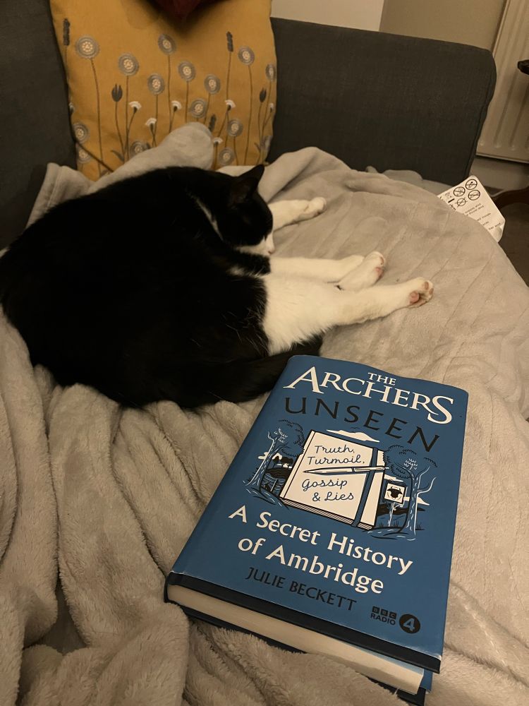 A copy of The Archers Unseen and a black and white cat 
