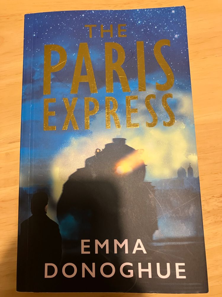 A copy of The Paris Express by Emma Donoghue. Cover shows the front of a steam train with a single beam of light from its middle.