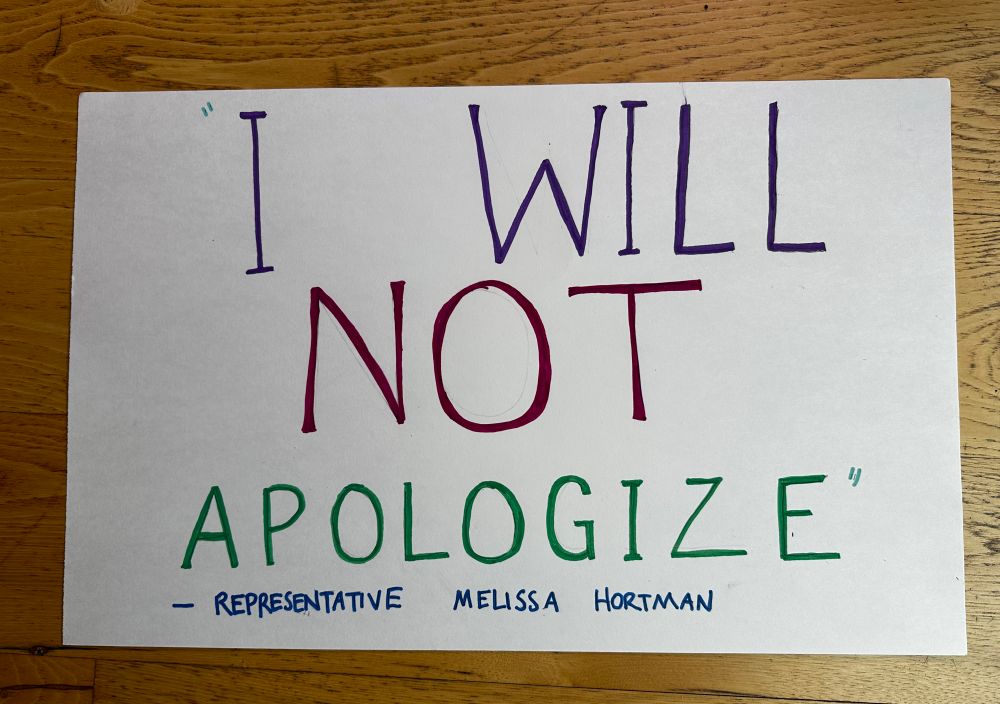A hand-lettered sign reads “‘I WILL NOT APOLOGIZE’ -Representative Melissa Hortman”
