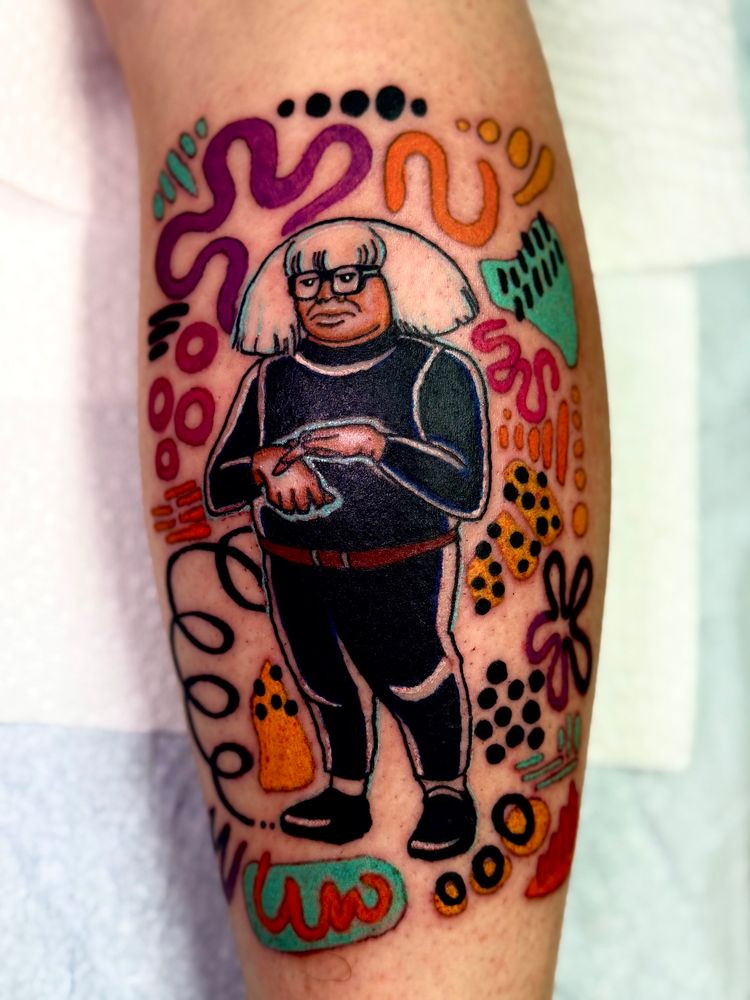 Color Danny Devito tattoo of him as Frank Reynolds wearing a white wig and black outfit with subjective art as a backdrop 