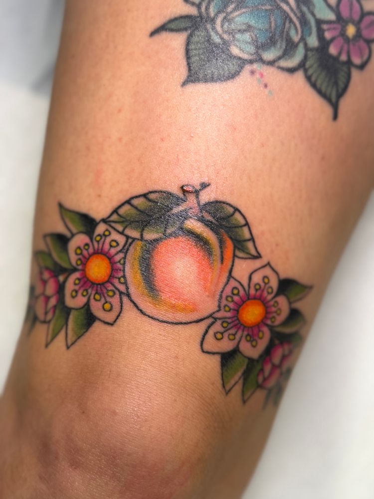American traditional tattoo of a peach with peach blossoms on a band above the knee 