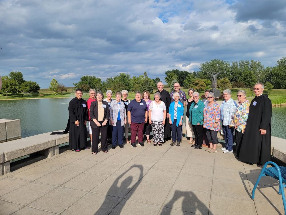 A group of men and women standing in front of a lake posing for a group picture. 