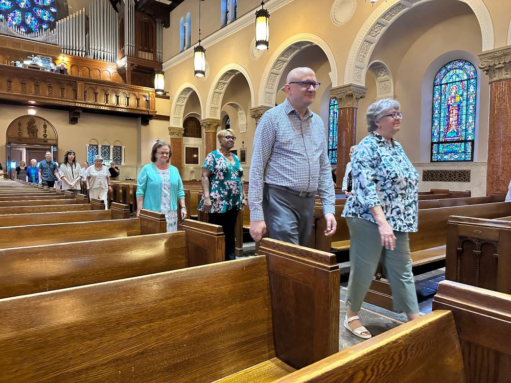A line of people walking two by two by two down the center aisle of a Catholic church. 
