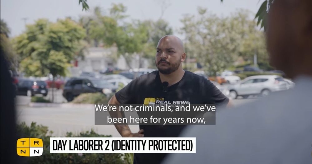 Screenshot from TRNN doc report showing Max listening to immigrant day laborers outside a Home Depot. Captions read "We're not criminals, and we've been here for years now..." 