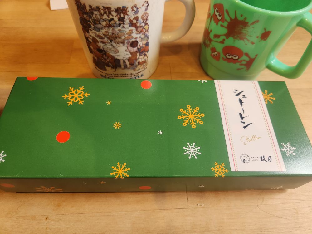 鼓月　シュトーレンの箱。緑地に金と白の雪の絵柄と赤い円が描かれ、縦書きで「シュトーレン」と書かれている。