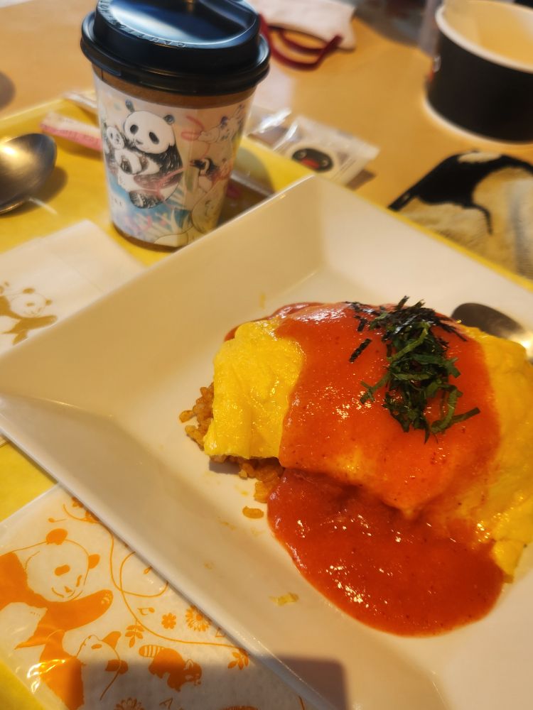 アドベンチャーワールドの明太子オムライスとカフェラテ。カップスリーブ、お手拭きとペーパーナプキンにパンダが描かれている。