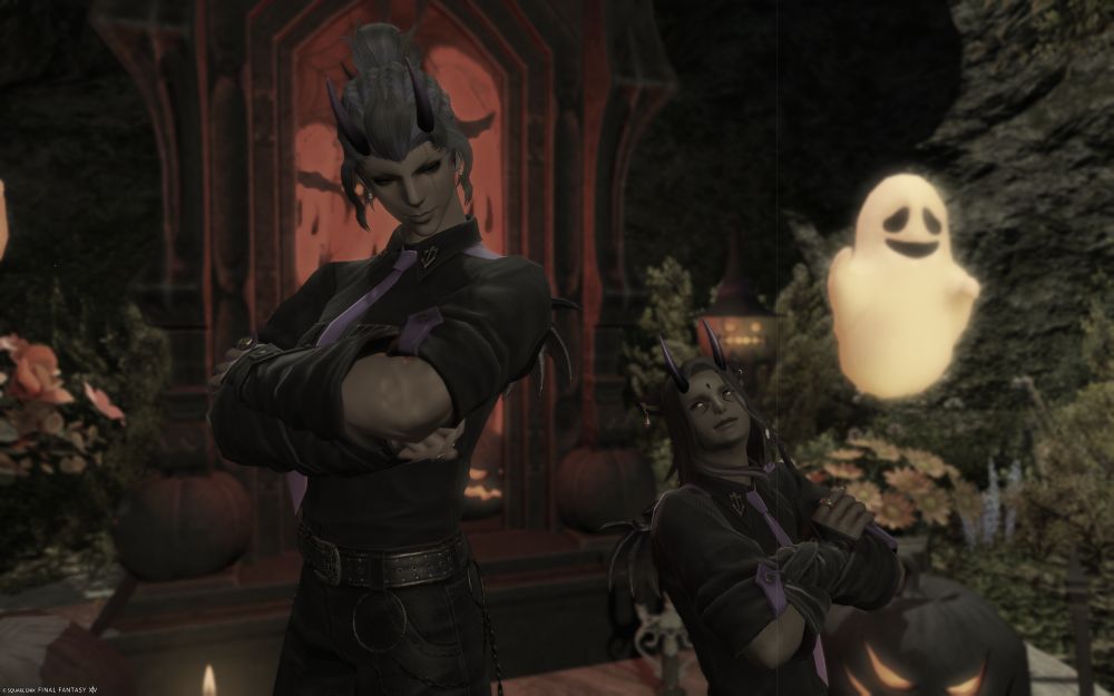 A tall Roegadyn woman and a shorter Miqo'te man, both dressed in black and purple attire, stand back to back with their arms crossed and looking back at each other. Behind them is a Halloween displa of pumpkins, flowers, ghosts and a crypt. The interior of the crypt glows red.