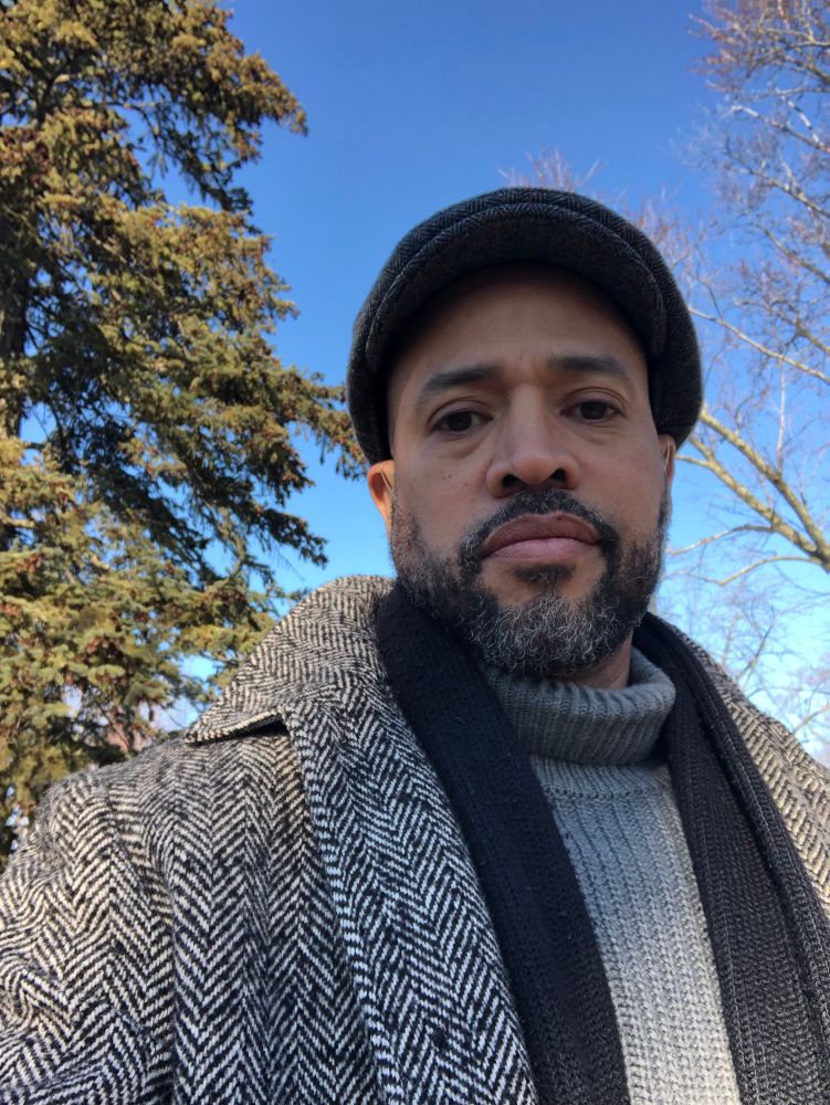 Selfie looking fly in my grey turtleneck sweater, black scarf, herringbone coat and wool newsboy cap. Background is beautiful blue sky with tree tops on both sides. 