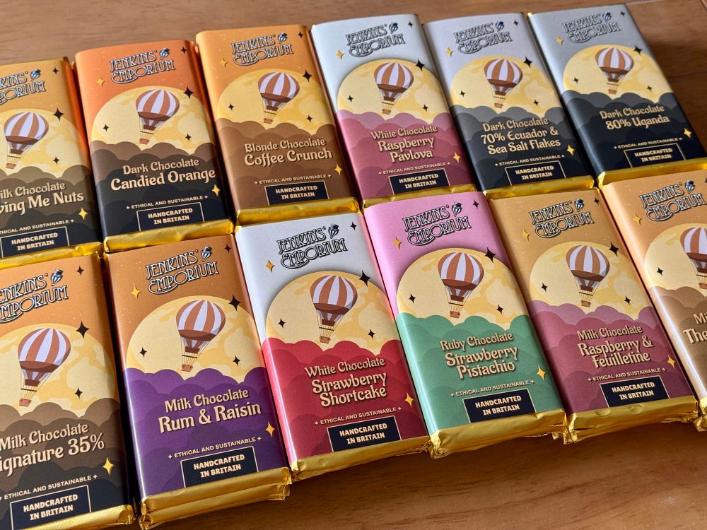 Piles of chocolate bars lined on a wooden table, ready to be packed and shipped! The packaging features a hot air balloon hovering in front of a moon, with clouds of different colours underneath.