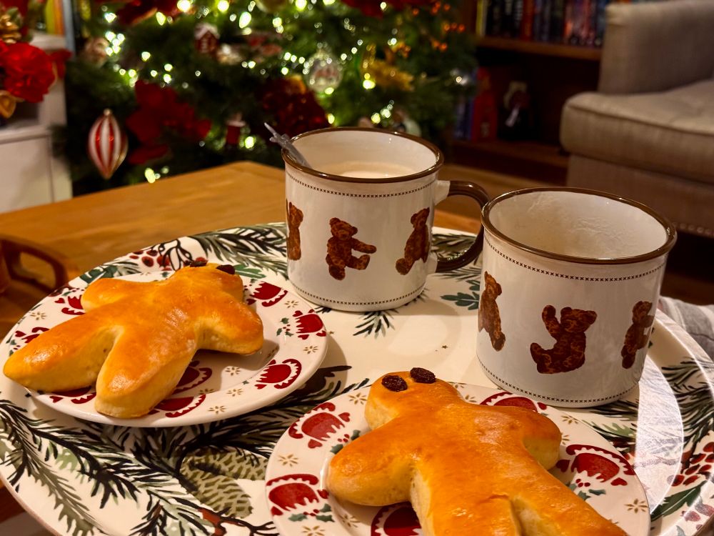 A tray with some mannelle (st nicholas brioche, people shaped) and coffee mugs. Christmas tree in the background.