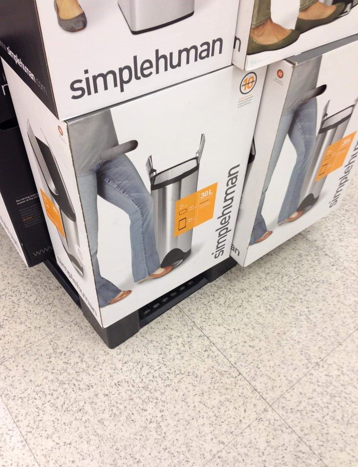 The packaging of a trashcan. The lower body of man is next to the trashcan on the box. A handle to carry the box is misplaced and look like the man's penis.