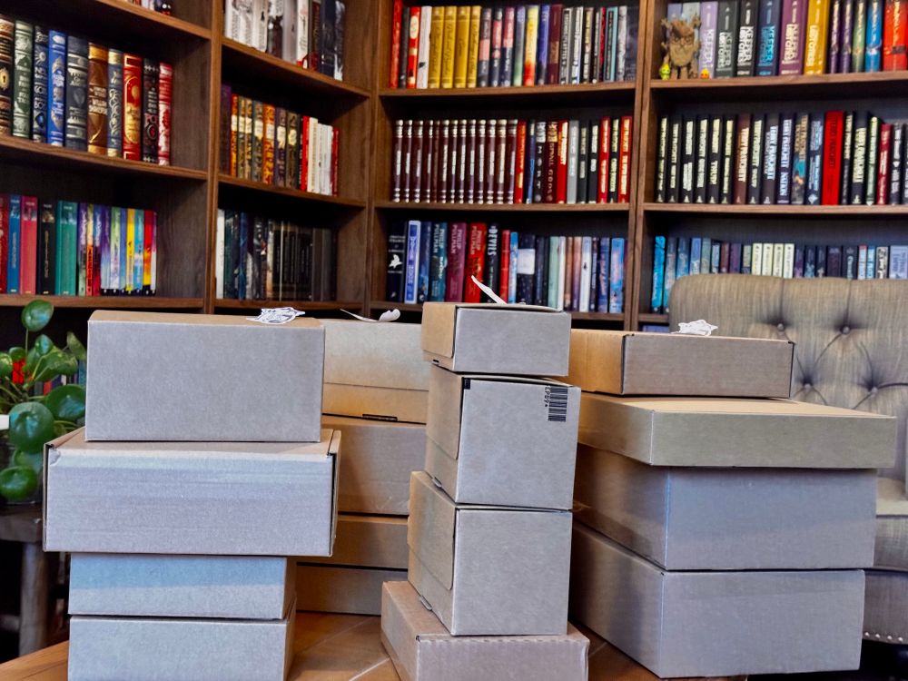 Many parcels on a wooden table. Bookshelves in the background.