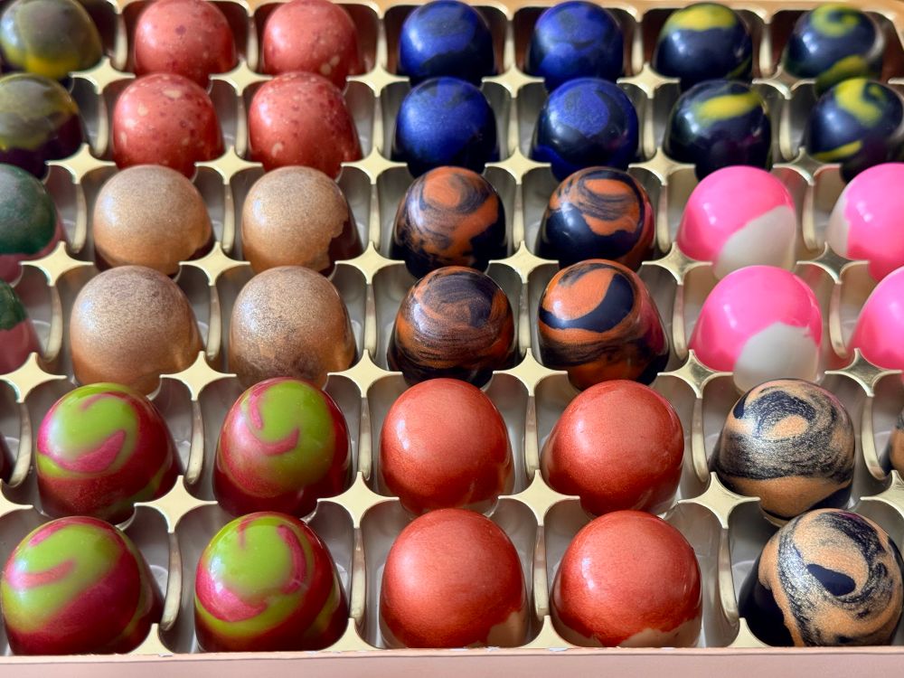Rows of small shiny chocolates of various colours sitting in a golden box