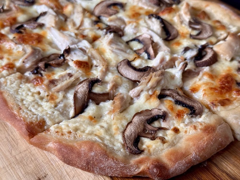 A golden pizza with a creme base, chicken, and mushrooms.