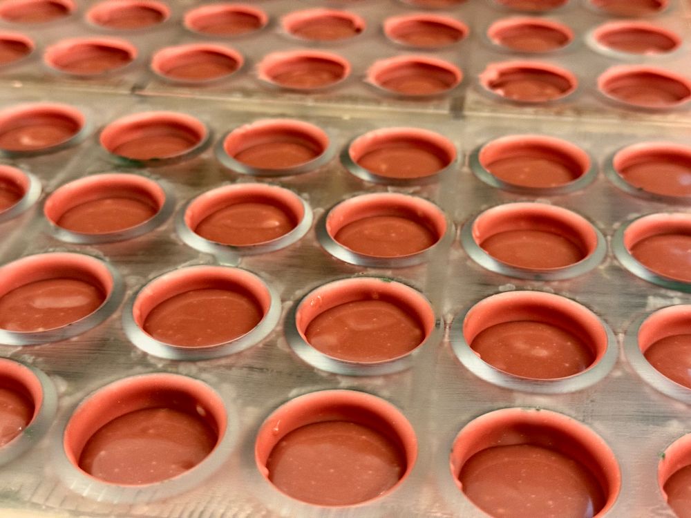 Many rows of pink-red chocolate in their moulds. A layer of ruby ganache visible.