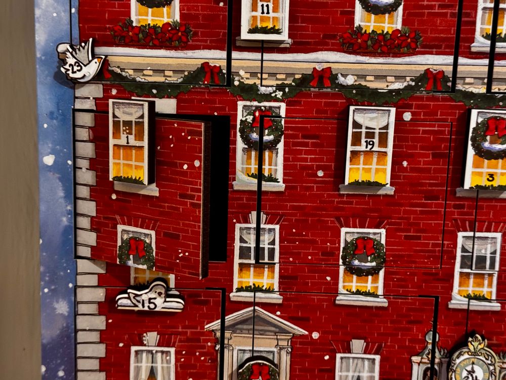 An advent calendar (a red brick house with many windows decorated for Christmas). The door with the 1 on it is ajar.