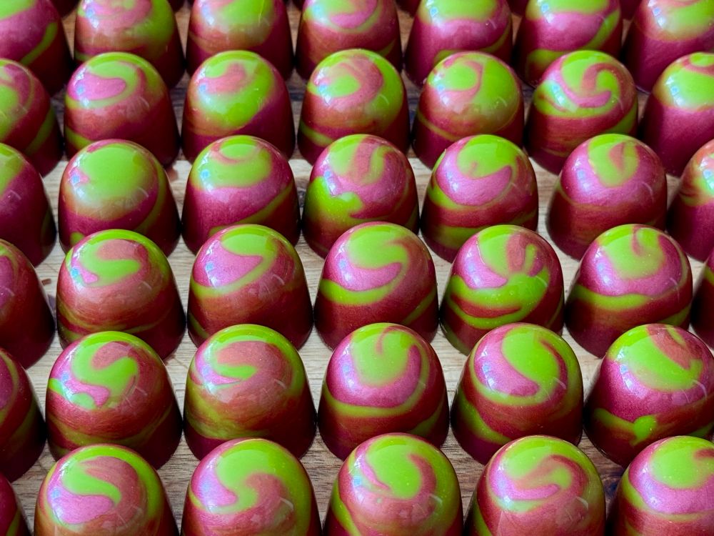 Rows of shiny chocolates decorated with a green and red swirl.