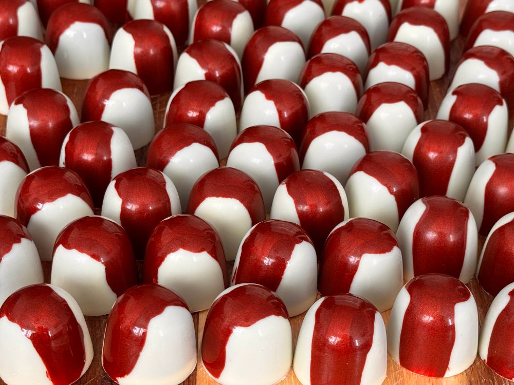 Many rows of shiny, white and maroon, chocolates 