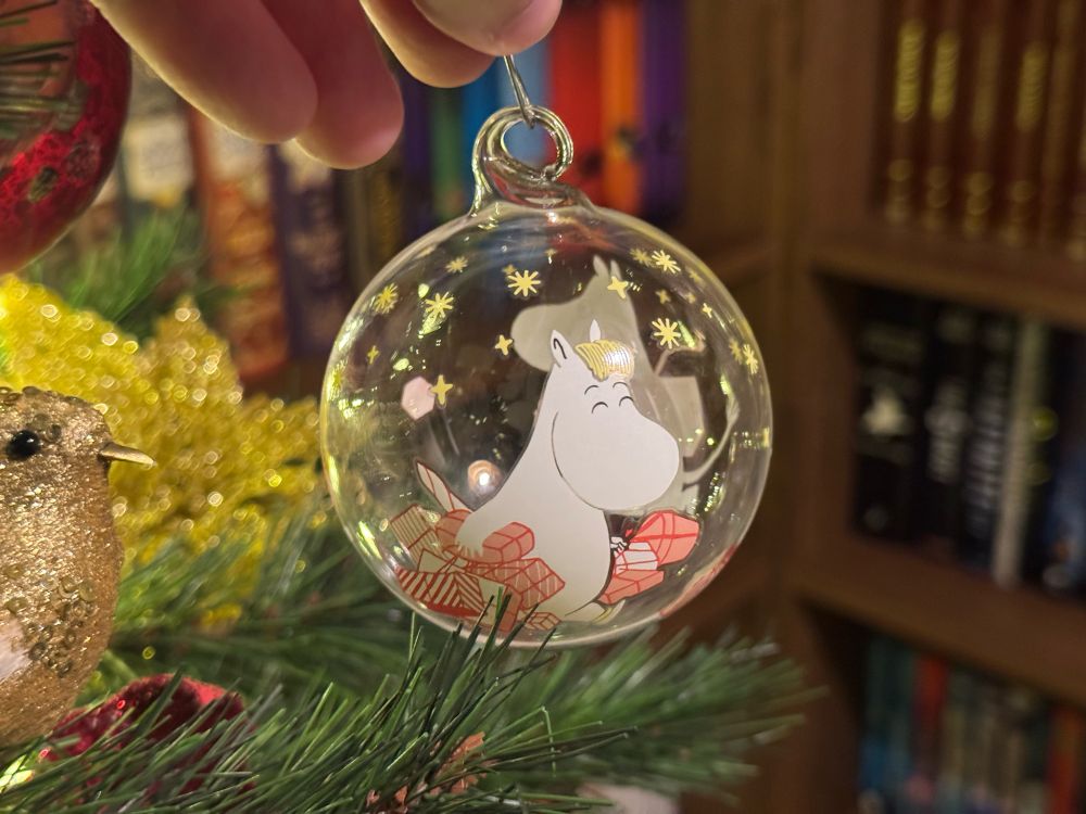 A Moomin bauble about to be put on a Christmas tree.