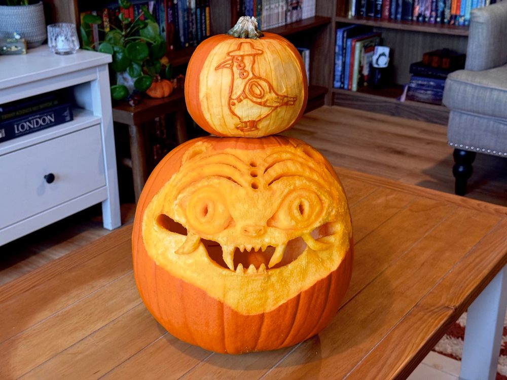 A pumpkin carved as a demon tiger (Derpy from Kpop demon hunters). A smaller pumpkin on its head with a demon crow carved in it (sussie)