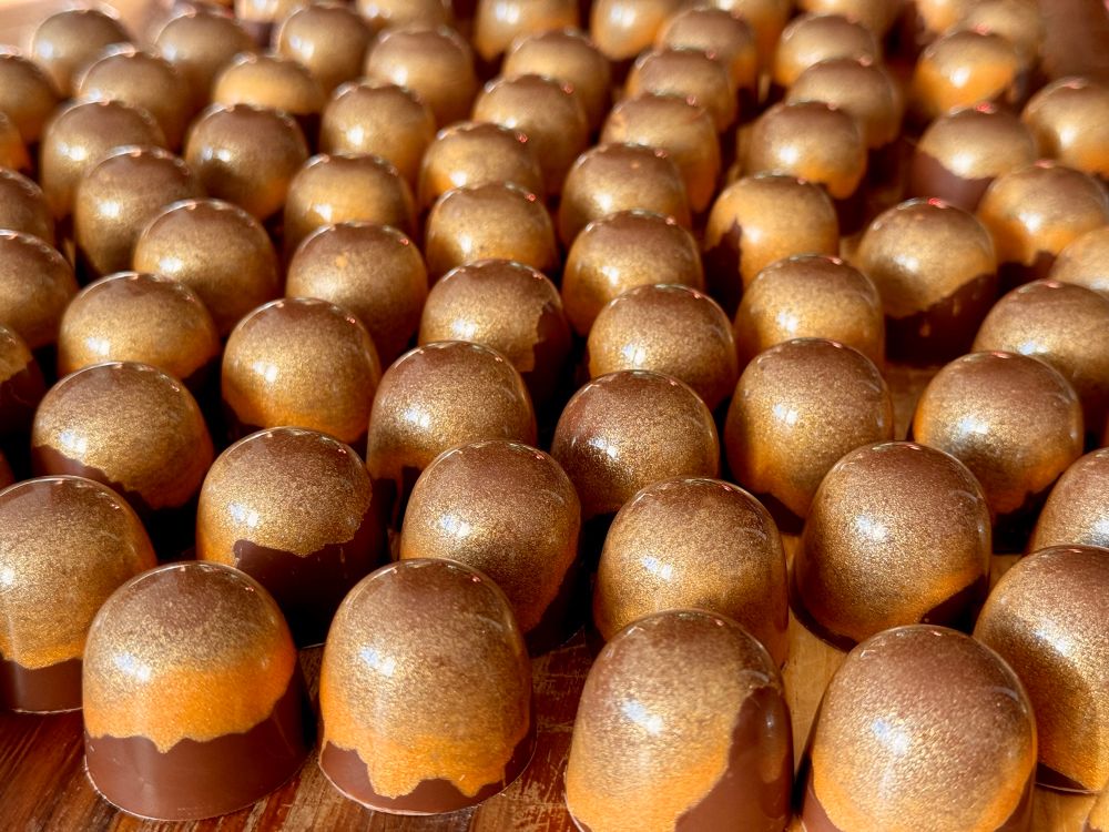 Many rows or shiny gold and brown chocolates.