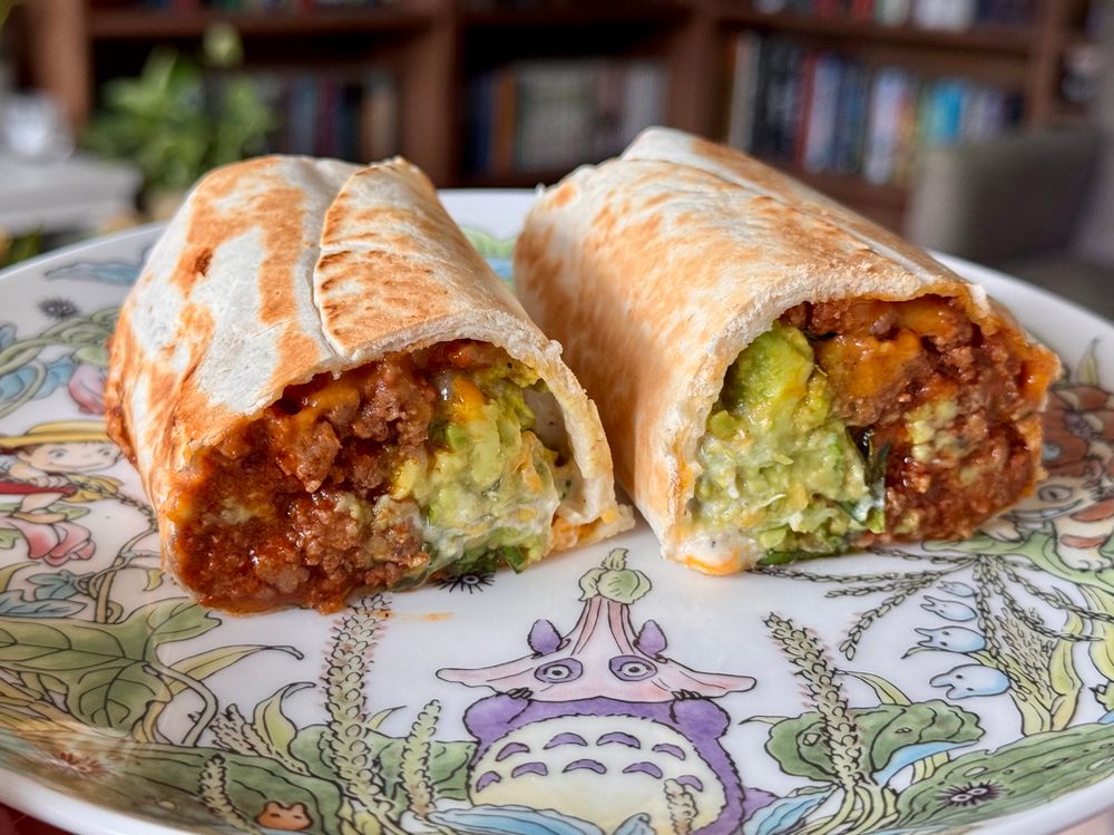 Two half burritos on a totoro plate. They are filled with guacamole, lettuce, cheese, and spicy tomato ground beef.
