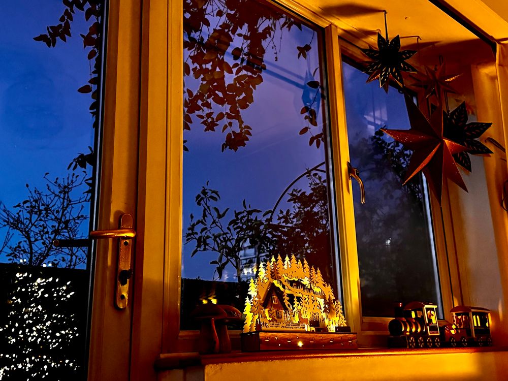 Christmas decorations lit on a windowsill. Dark morning sky outside.